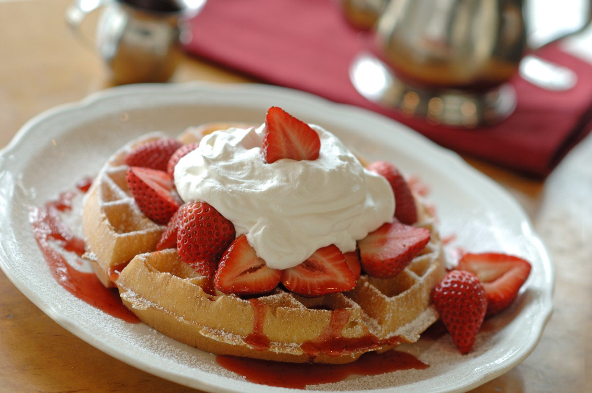 Waffle topped with strawberries and whipped cream, drizzled with syrup on a white plate.