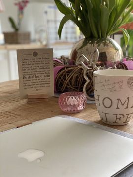 Auf einem Tisch steht ein Laptop neben einer Tasse mit der Aufschrift „Home Life“.