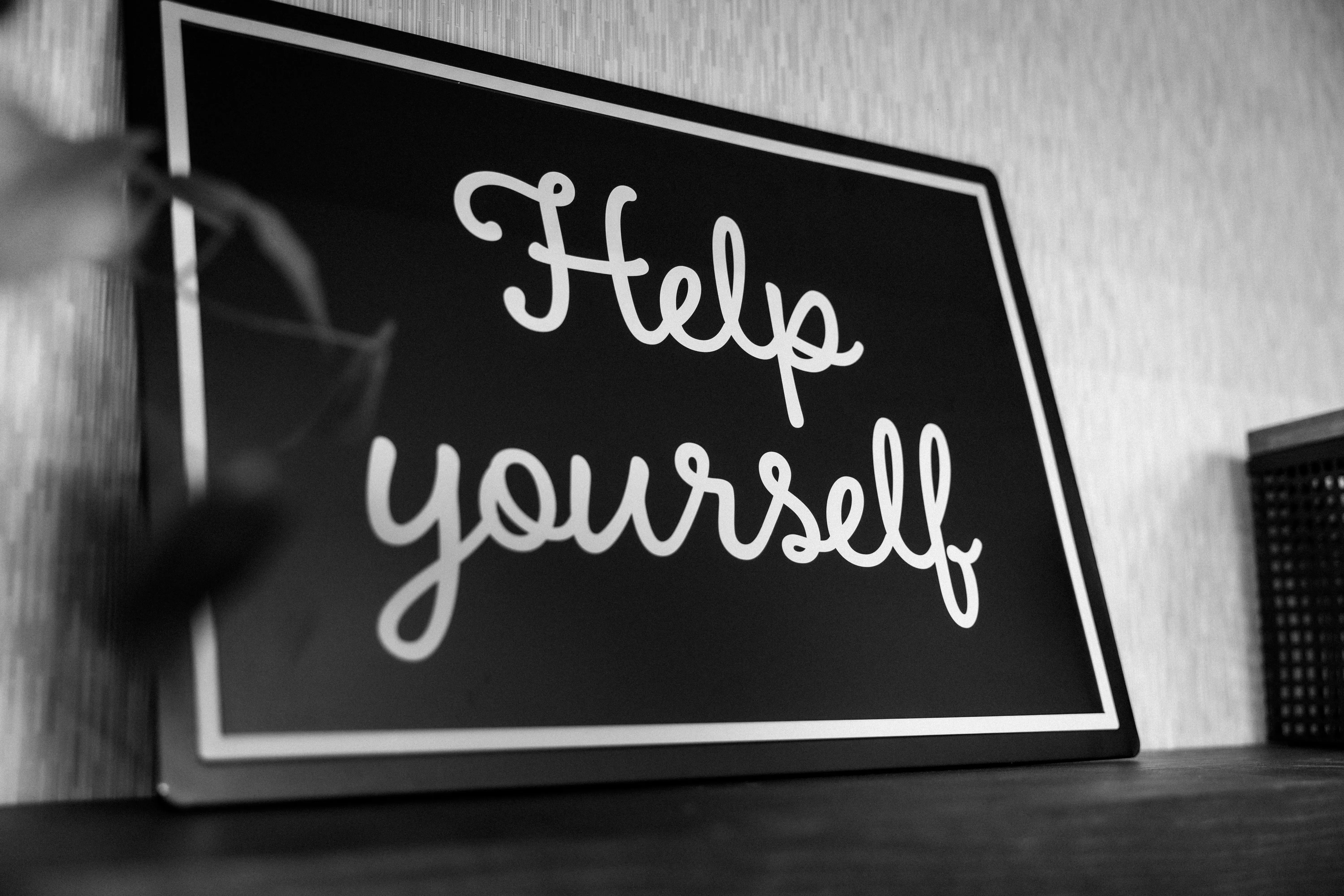 Black-and-white sign on a shelf reading “Help yourself”