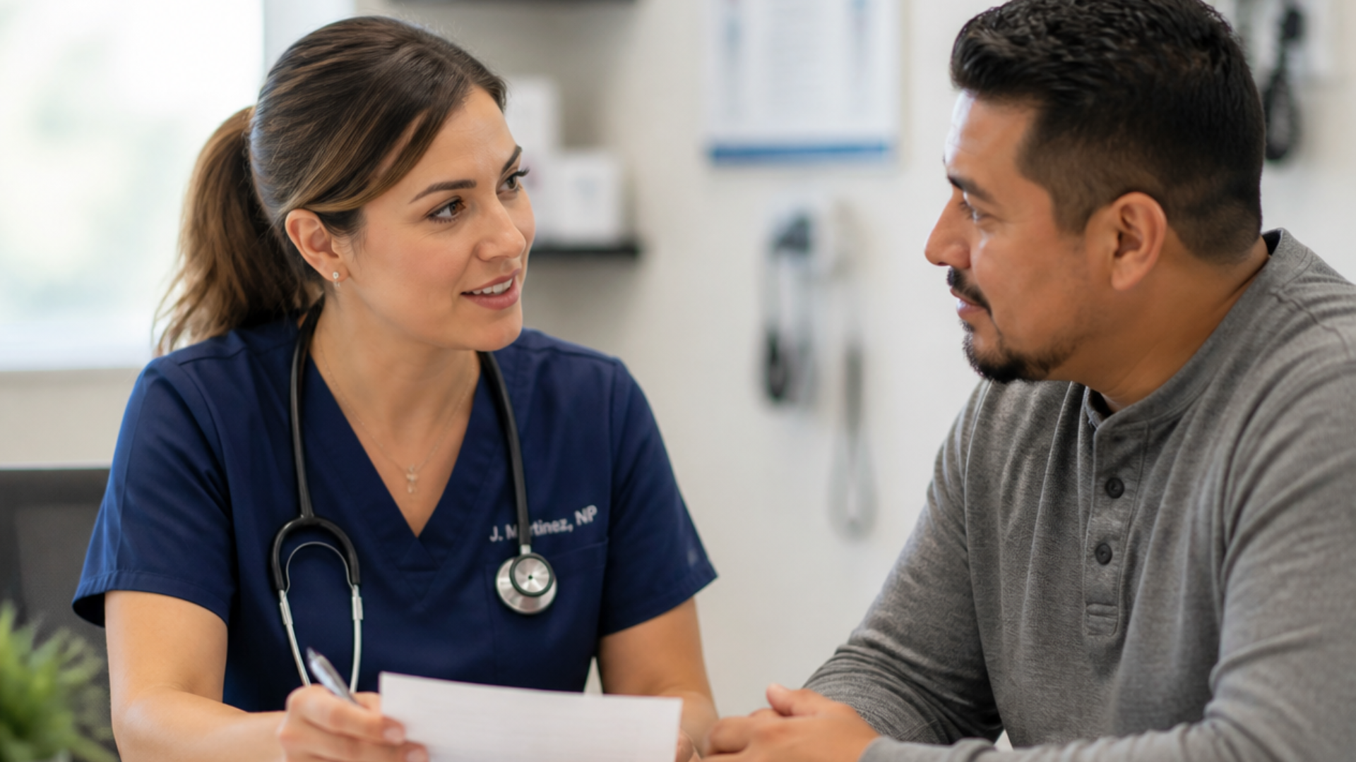 Nurse in navy scrubs talking with a man in a gray shirt at a clinic desk