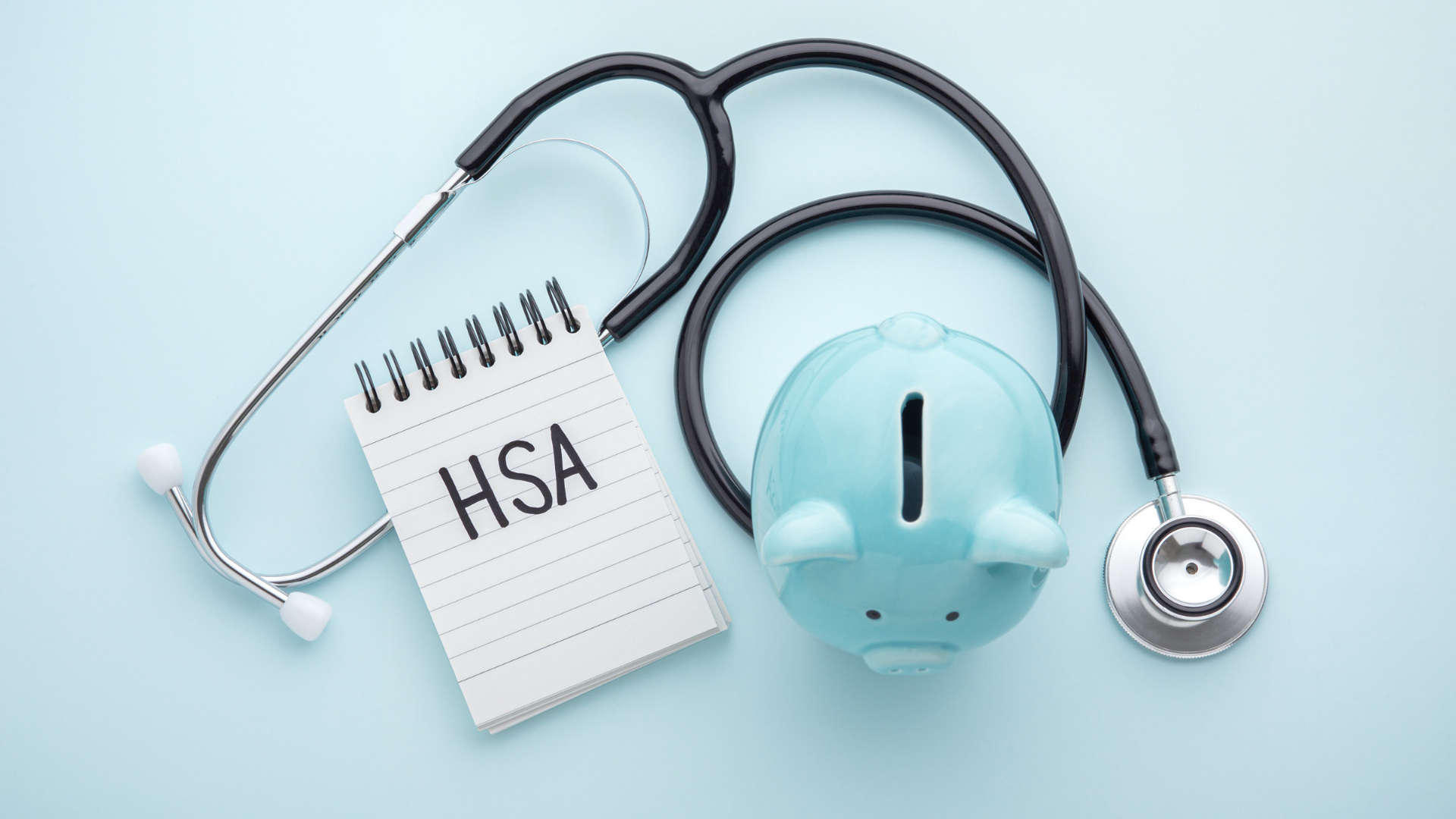 HSA notebook with stethoscope and light blue piggy bank on a pale blue background