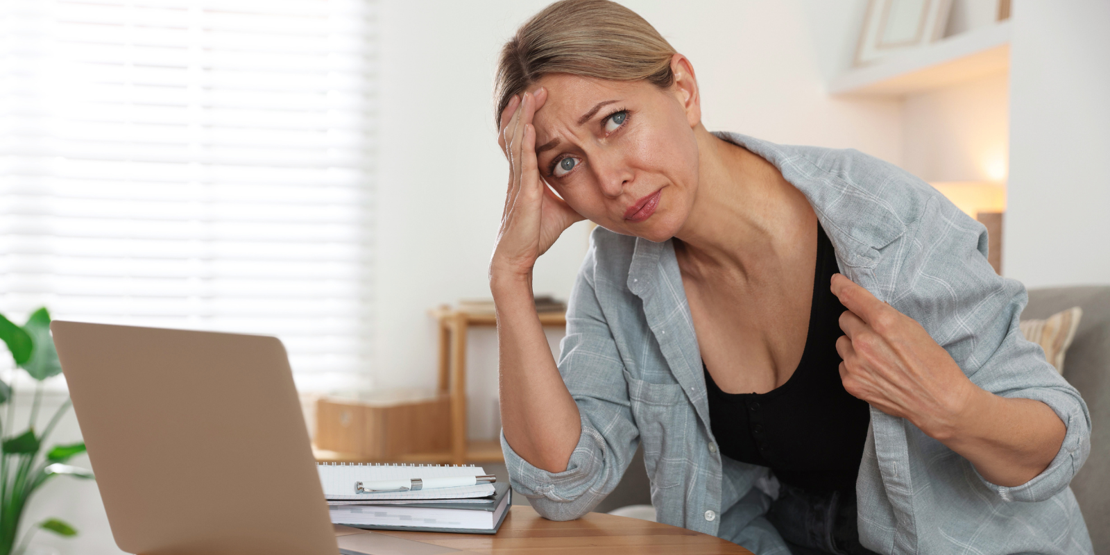 Woman in a gray cardigan sitting at a desk, looking tired and experiencing a hotflash while working