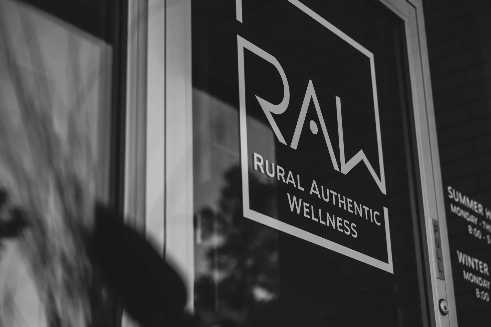 Black-and-white storefront sign reading “RAW Rural Authentic Wellness” in a window