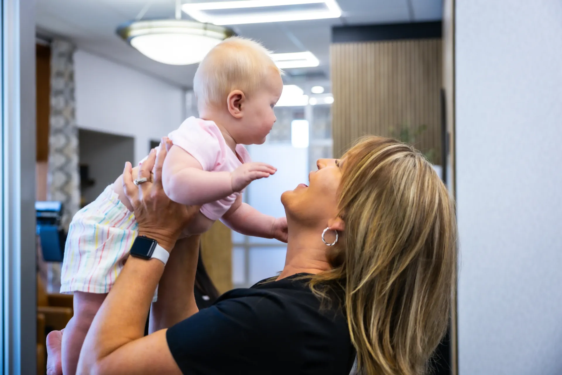 Adult holding baby up in a bright indoor room, smiling at the child.