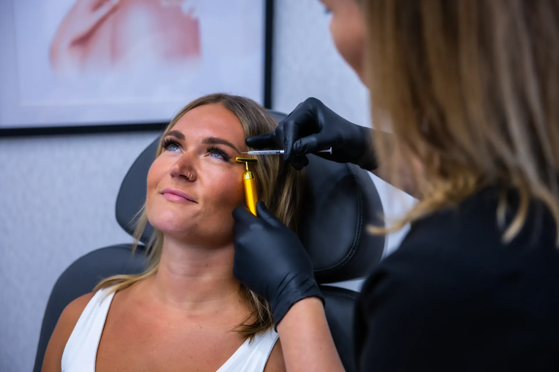 Cosmetic procedure on a woman’s eyebrow with a tool and yellow marking, in a clinic setting