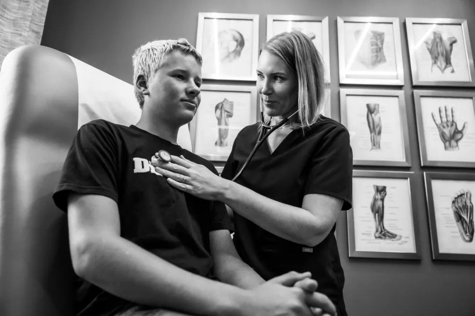 Clinician checks a seated patient in a room with framed anatomical drawings.