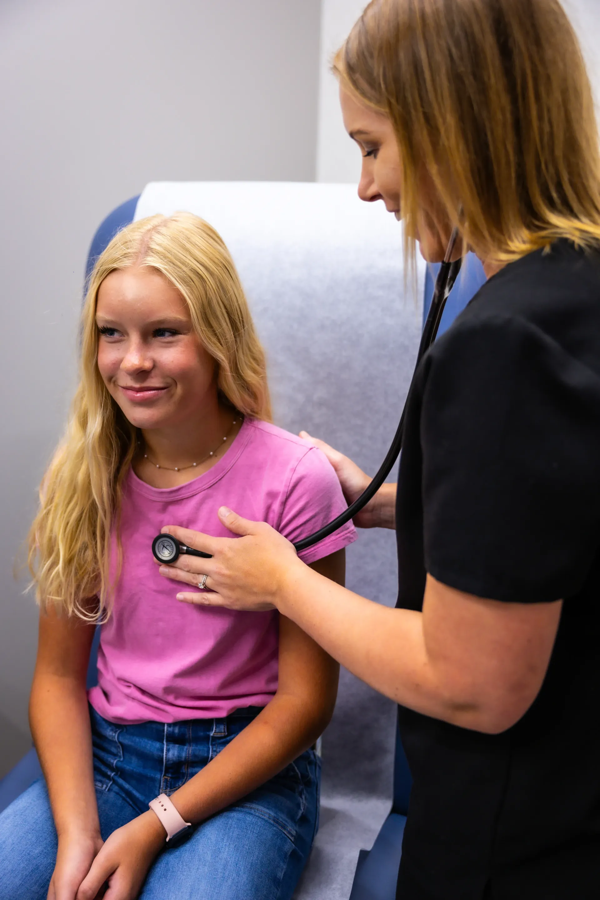 Doctor using a stethoscope to examine a seated patient in a clinic chair