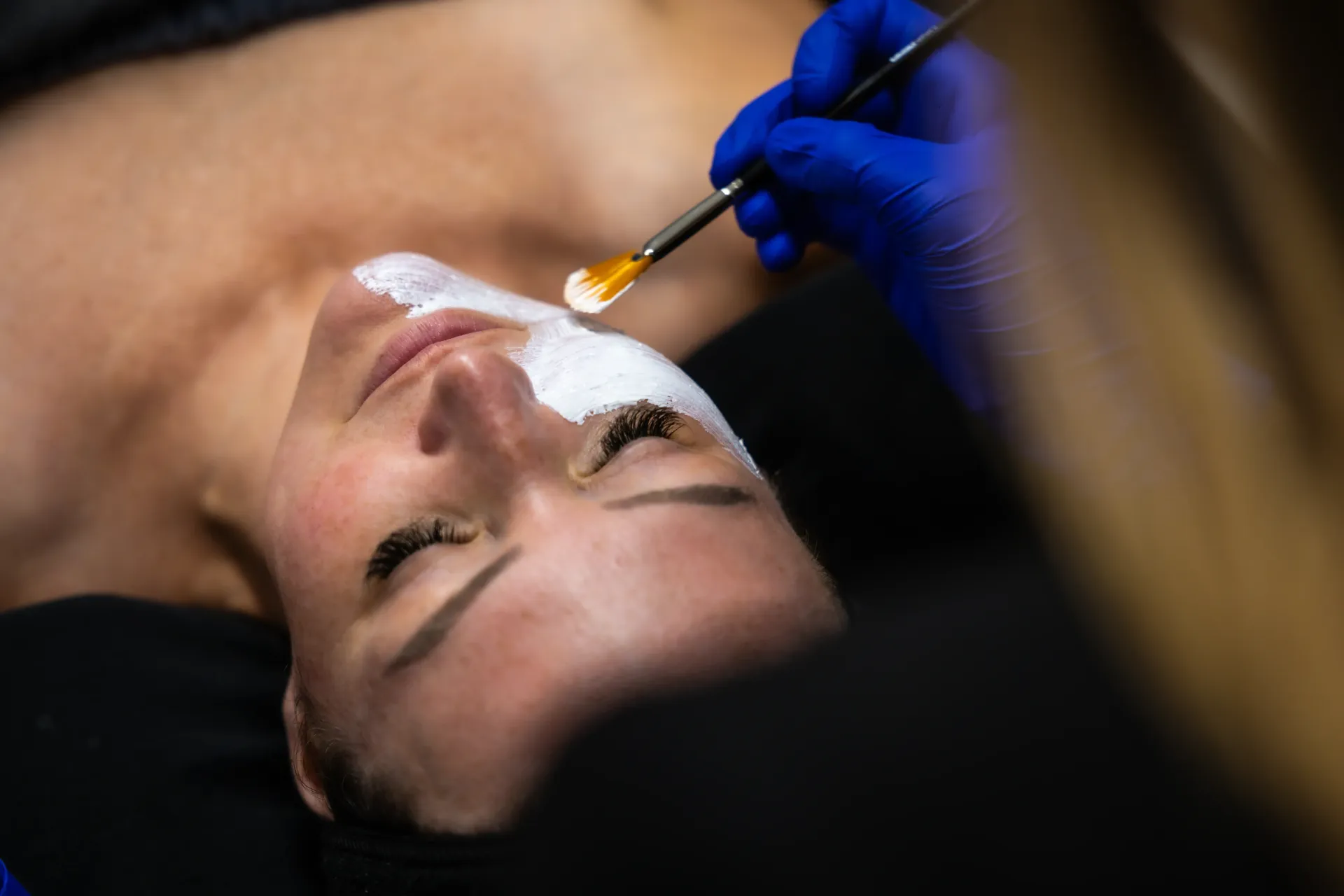 Person receiving a facial treatment with a brush applied to the nose and upper lip