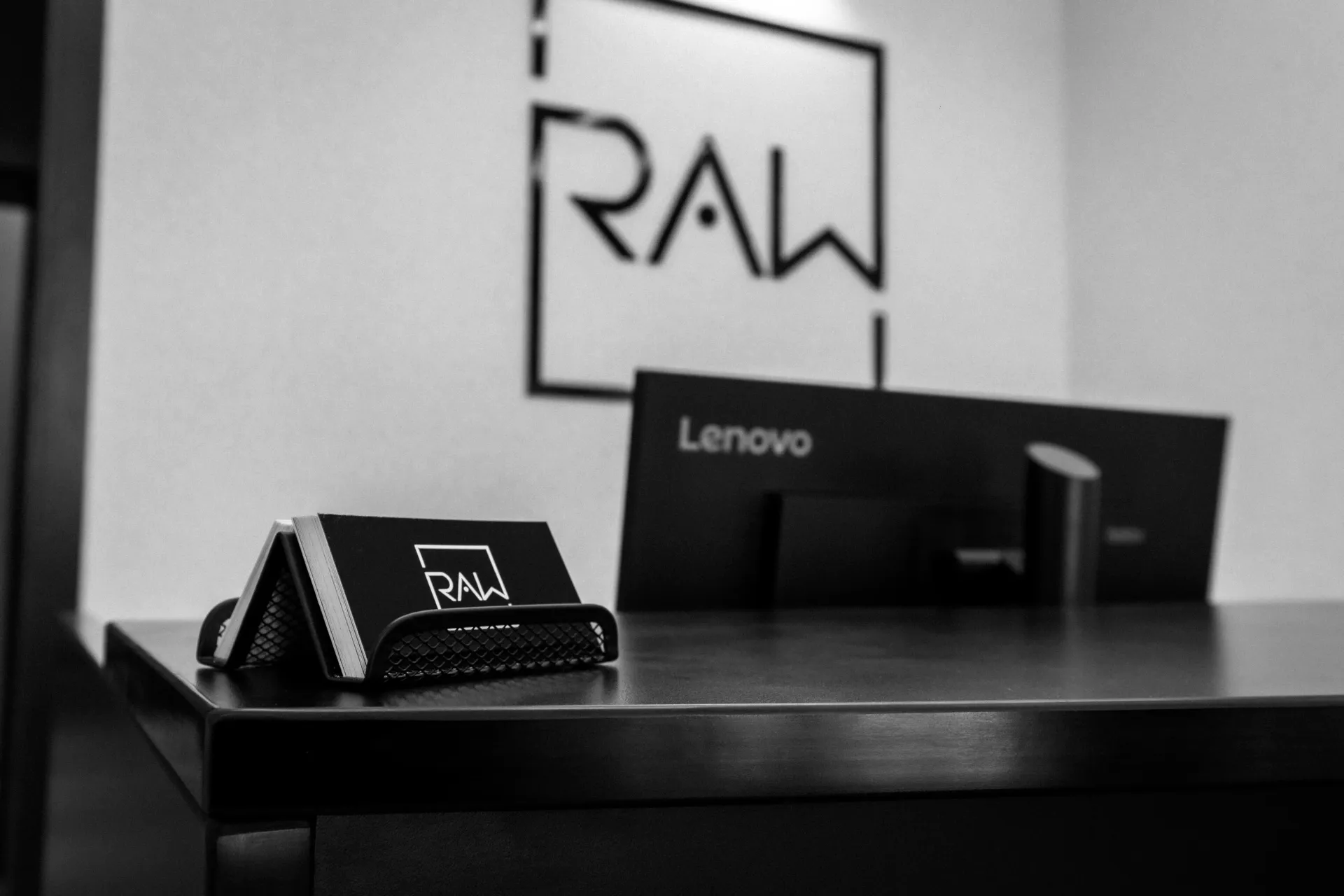 Black-and-white desk scene with RAW-branded items and a Lenovo box in the background