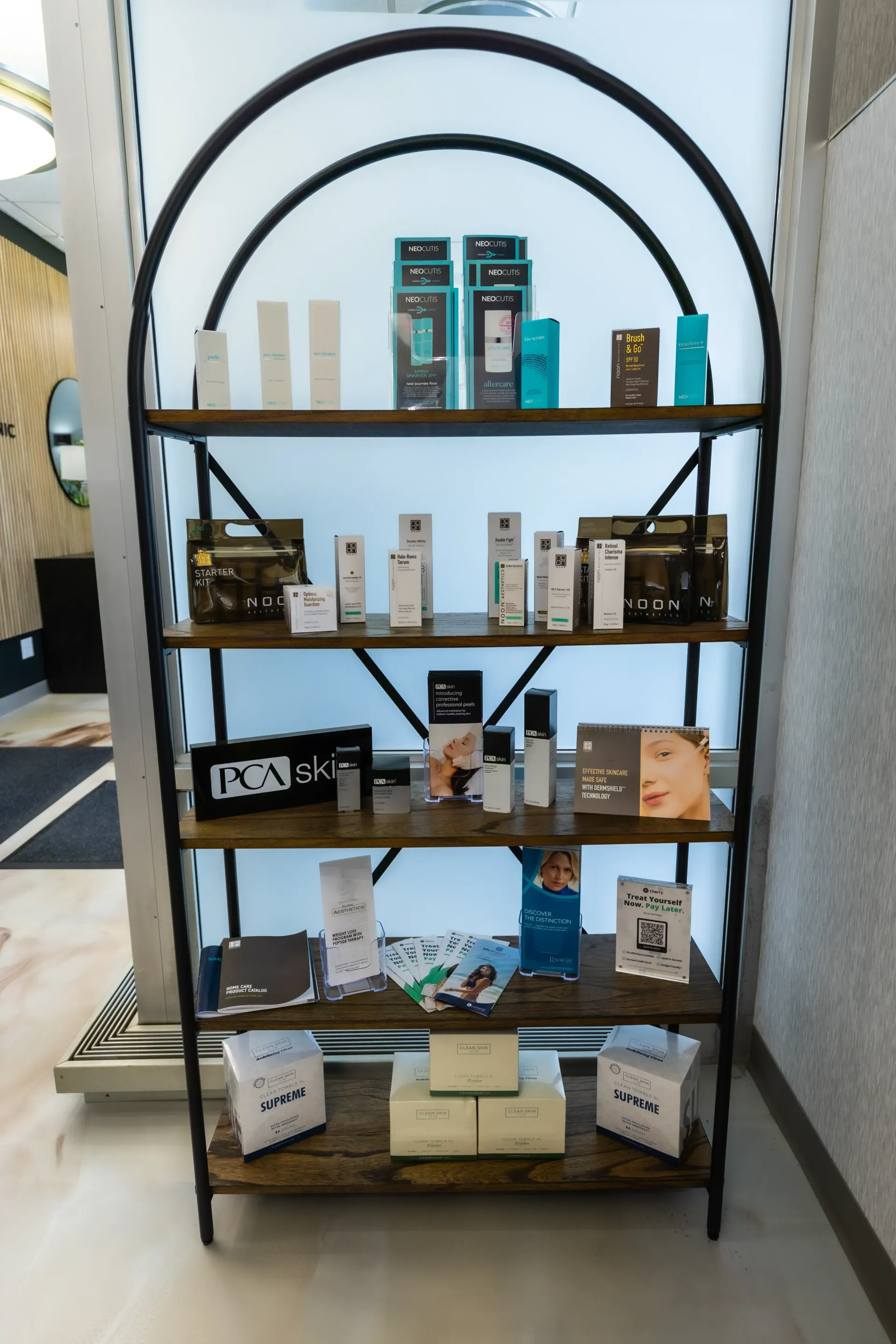 Black metal display shelf with assorted boxed products arranged on several wooden shelves in a store interior