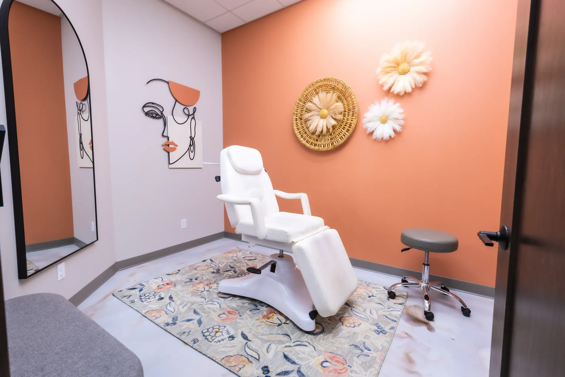 Modern treatment room with a white reclined chair, stool, mirror, and peach accent wall decor