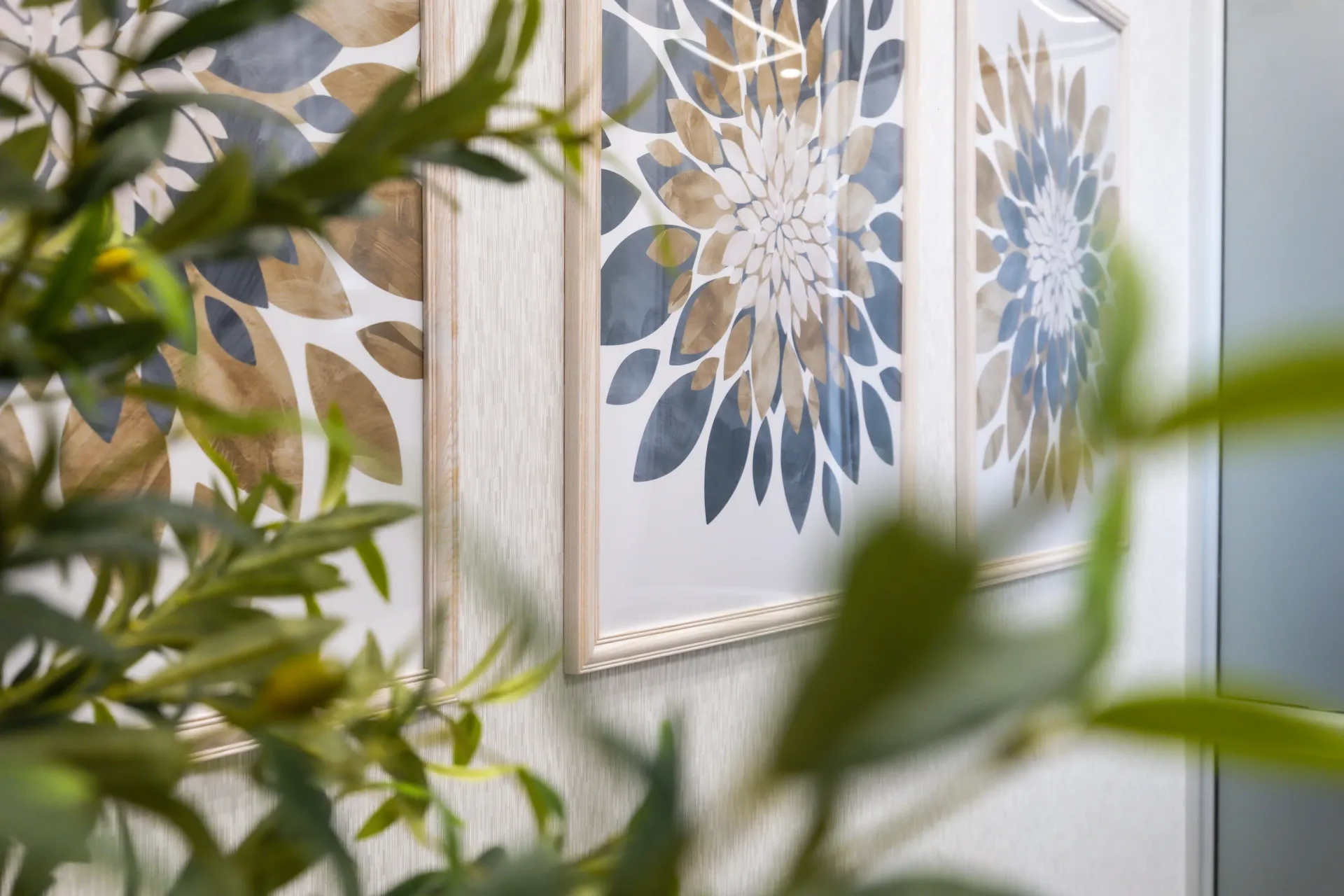 Framed floral prints on a bright wall, seen through blurred green leaves