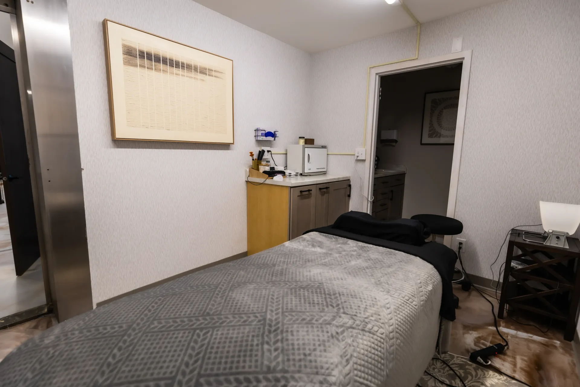 Small examination room with a bed, wall cabinet, sink, and doorway.