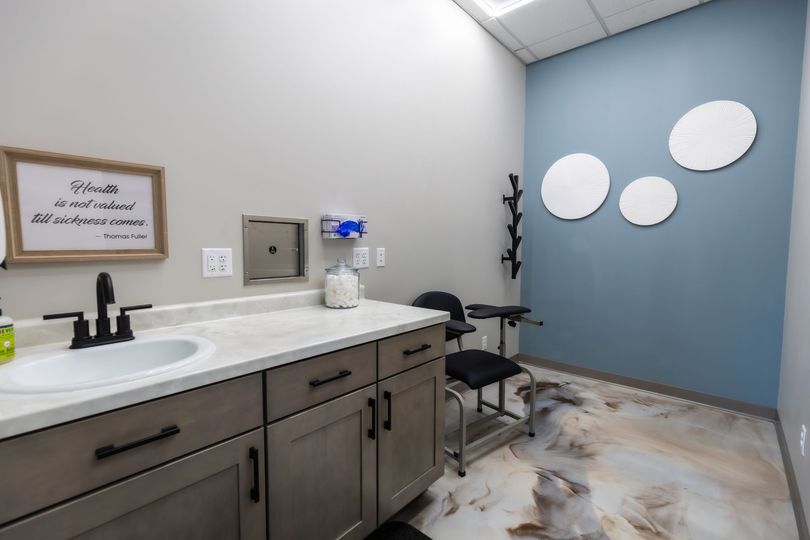 Modern treatment room with white chair, patterned rug, orange accent wall, and decorative wall art