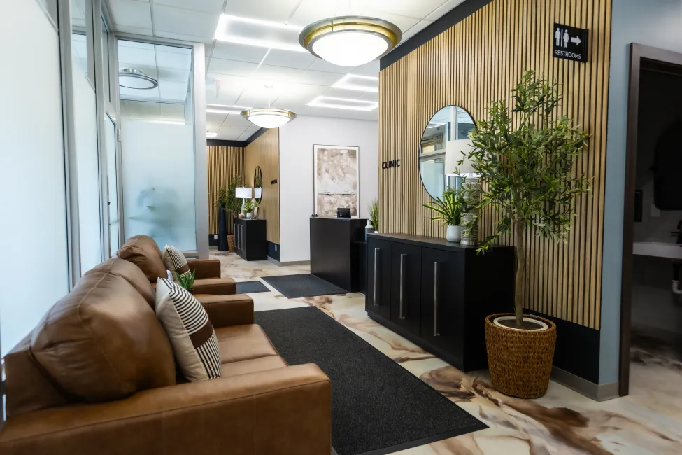 Modern hallway lounge with brown sofa, black console tables, striped wood wall, and potted plants