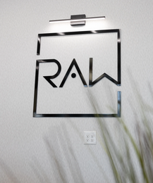 Black-framed wall art with the word “RAW” in stylized letters on a white wall.