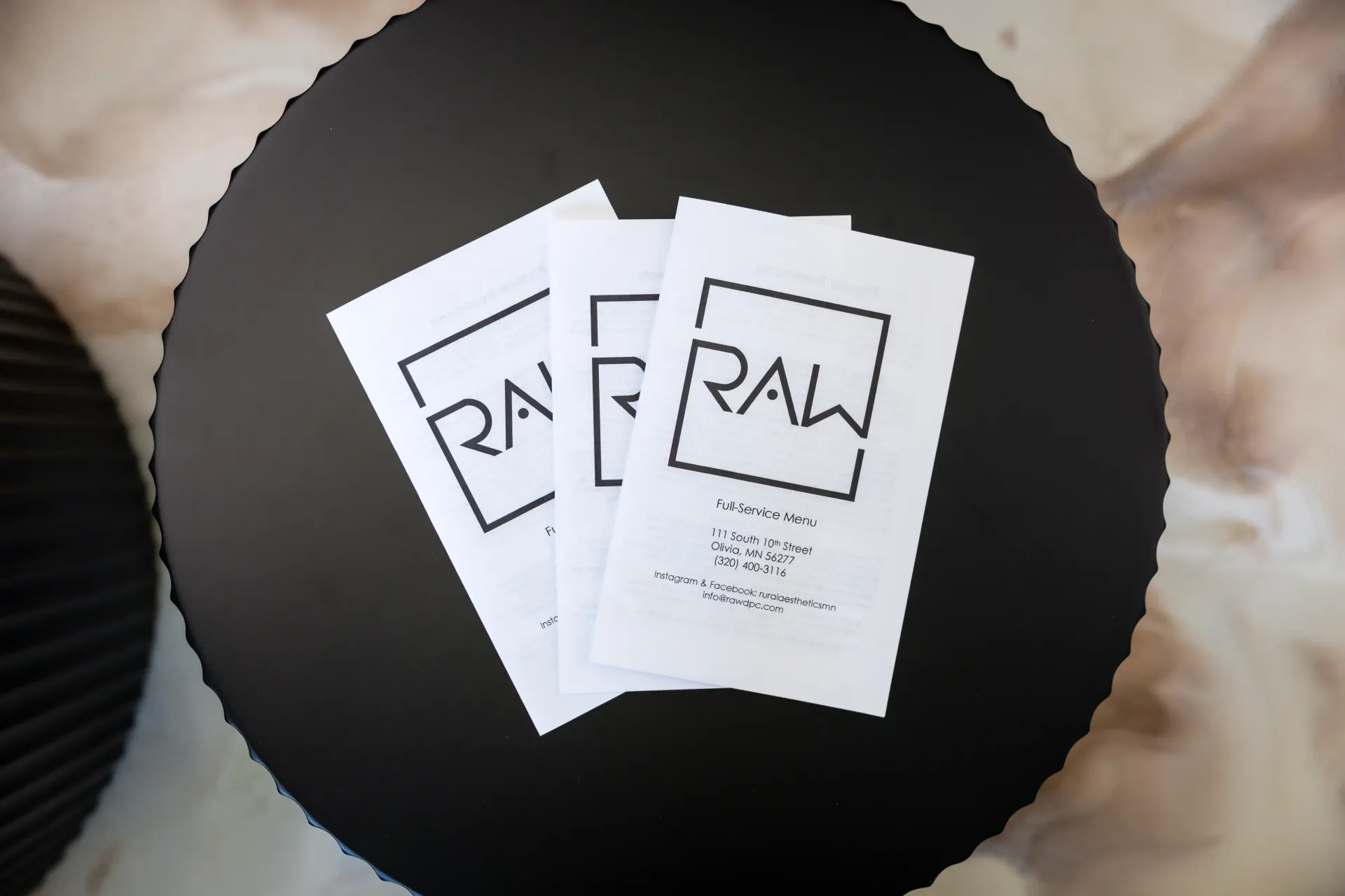 Two white RAW papers overlapping on a black circular surface, with beige fabric in the background