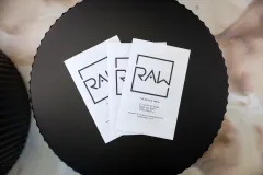 Three white RAW labels overlapping on a black circular surface.