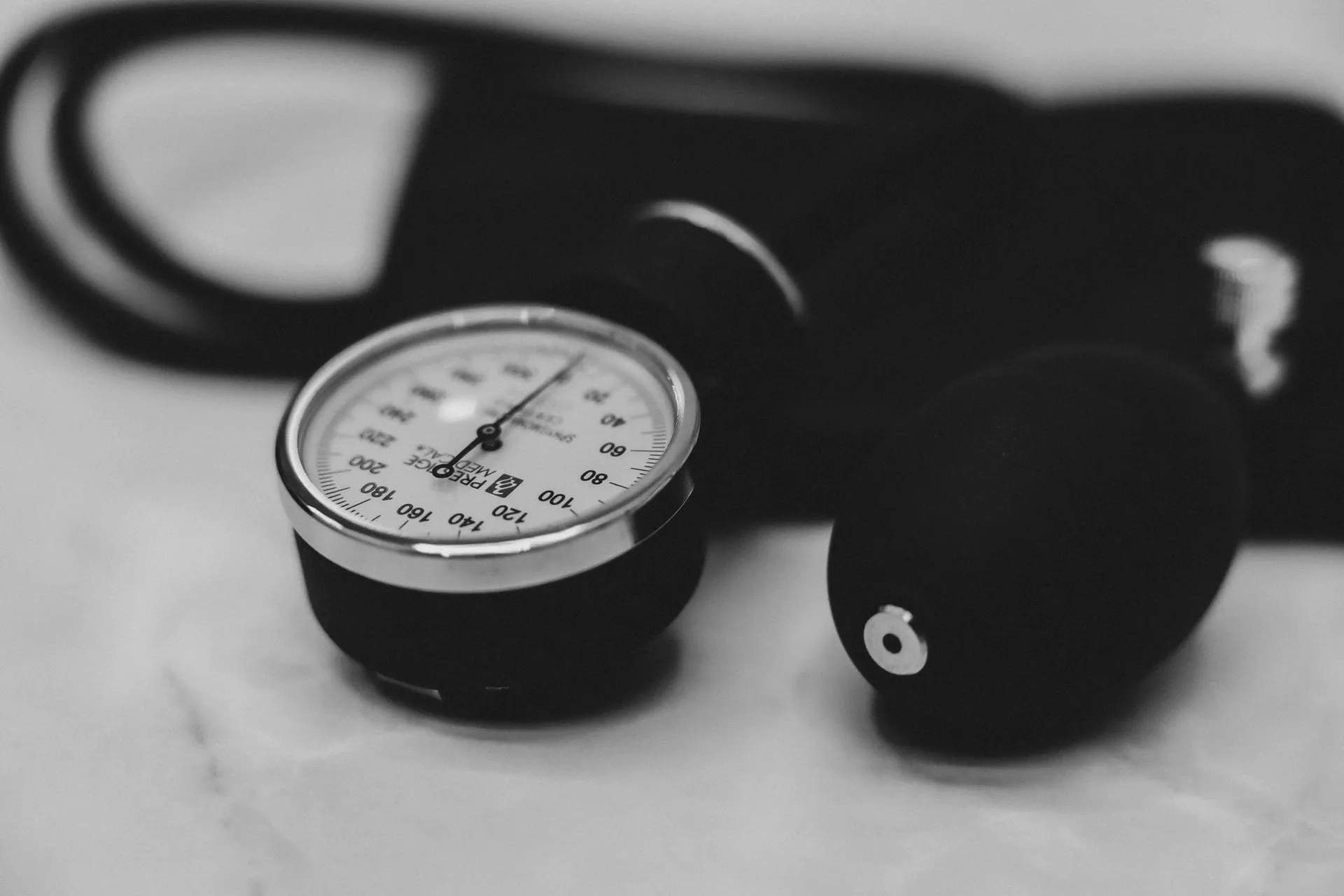 Black-and-white close-up of a blood pressure gauge and cuff on a light surface