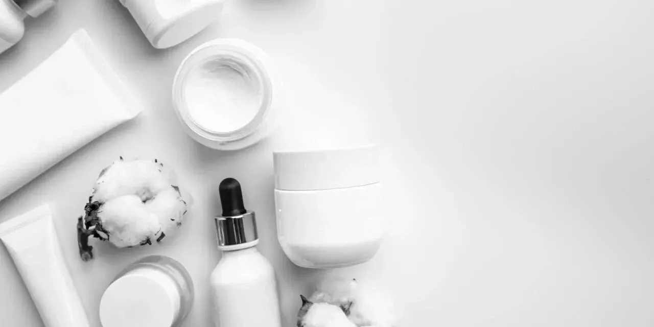Assorted white skincare bottles, jar, cotton, and dropper on a light background