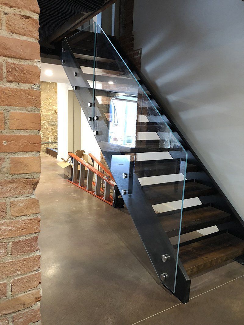Indoor staircase with glass railing beside a brick wall and gray floor