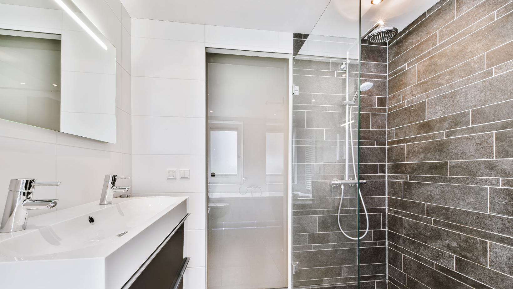 Modern white bathroom with vanity, mirror, frosted glass door, and tiled walk-in shower