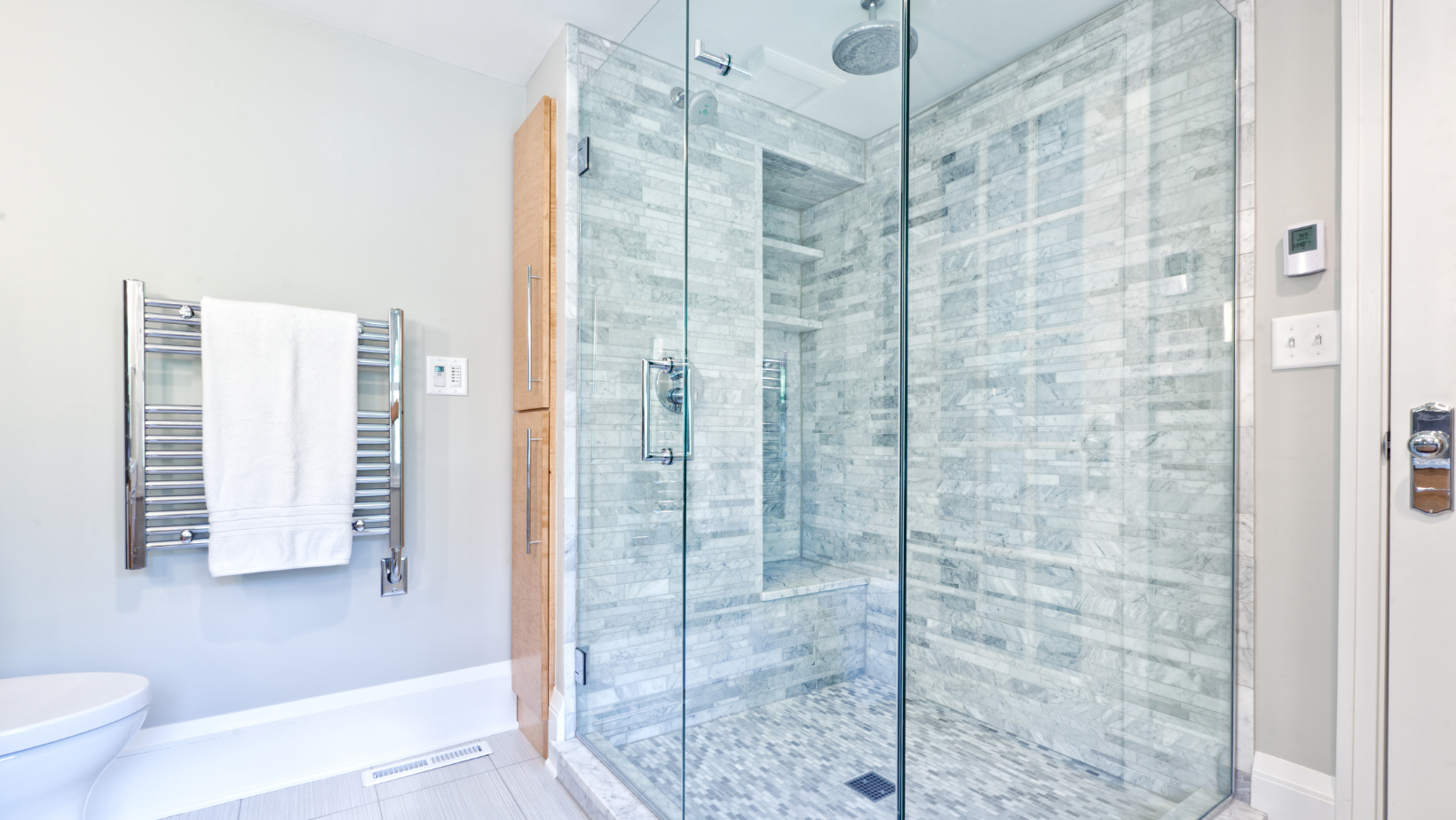Bright bathroom with a glass-enclosed tiled shower and a towel rack beside a bathtub