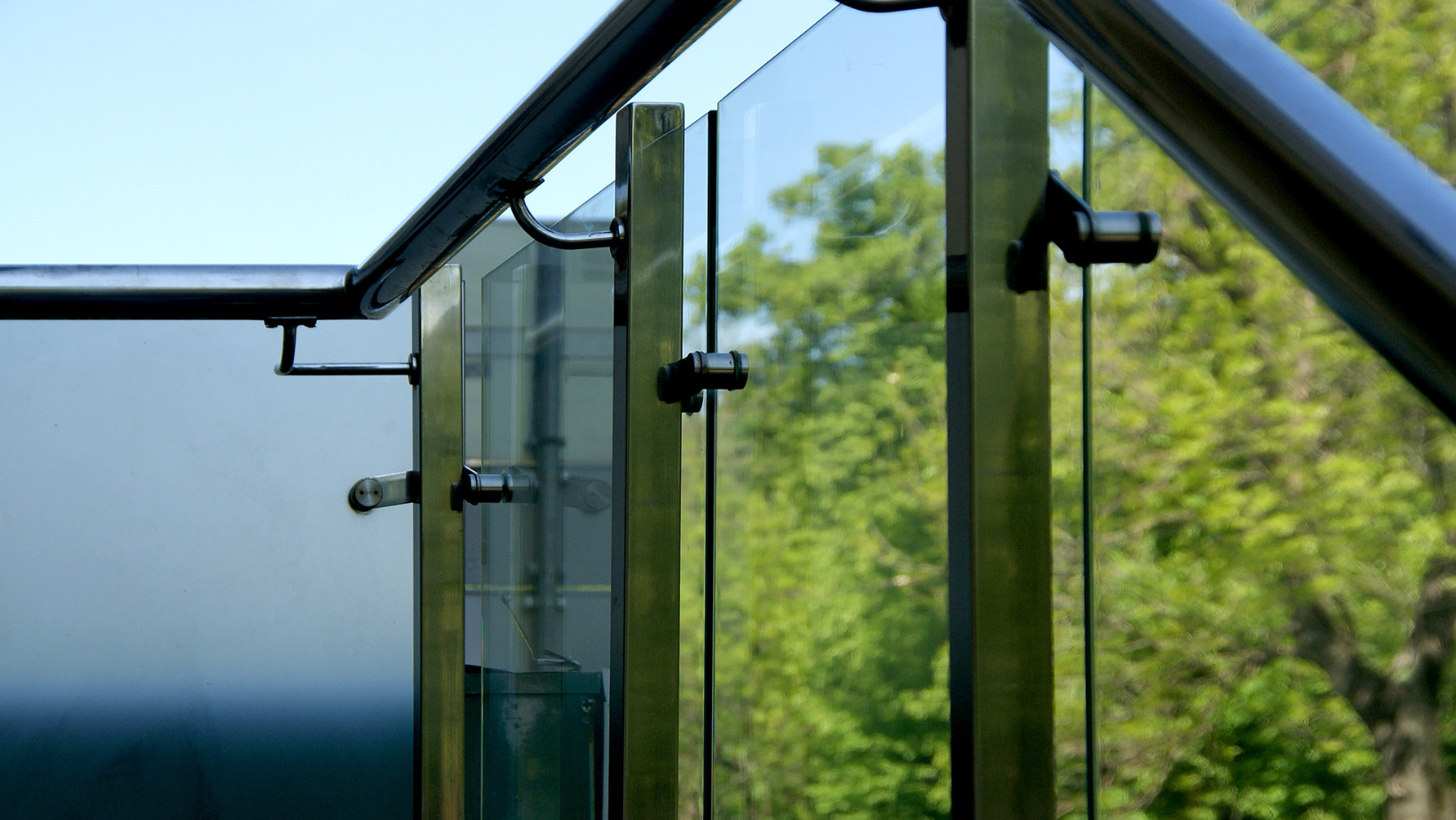 Glass balcony with metal frame overlooking green trees and blue sky