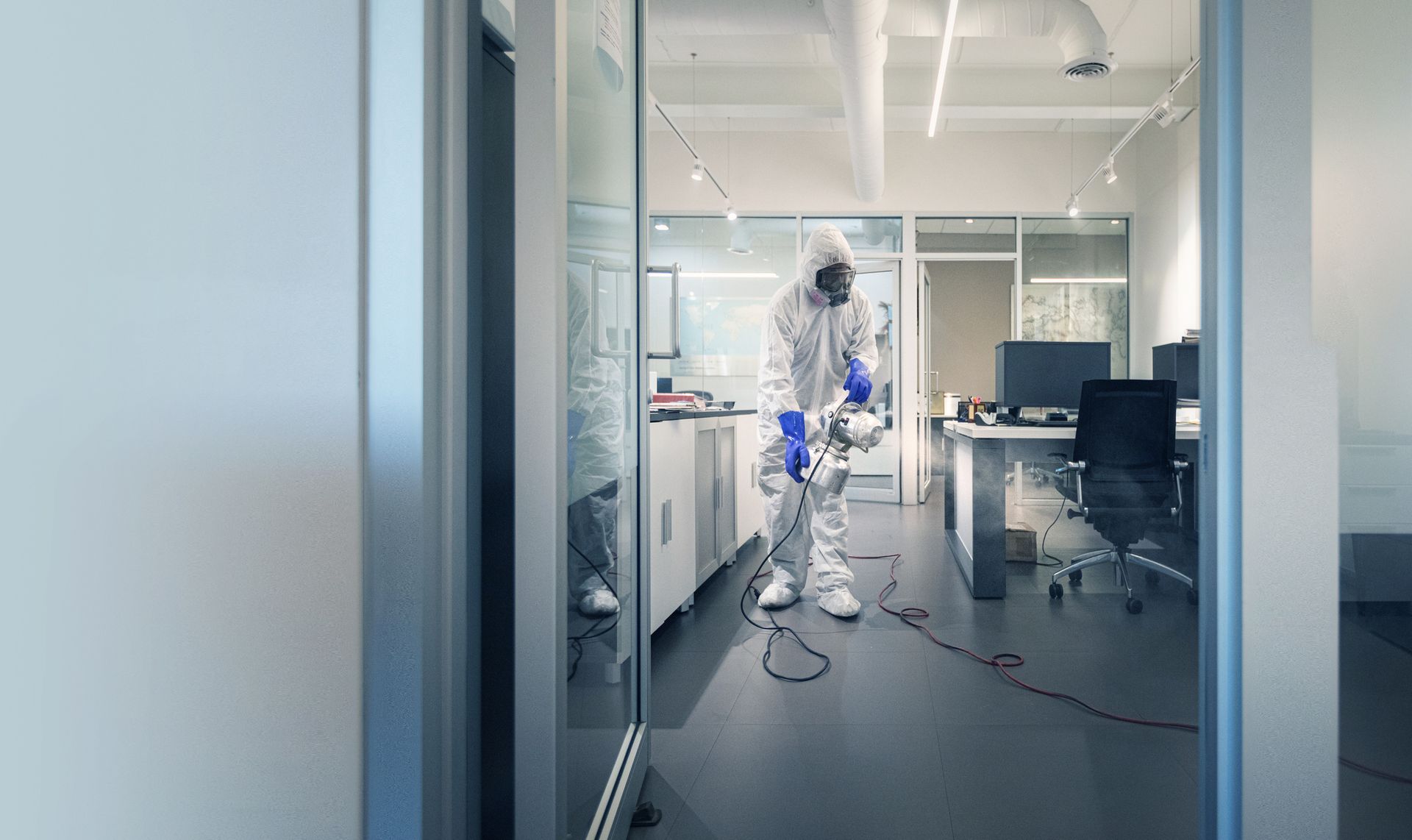 Person in hazmat suit disinfecting an office with a sprayer.