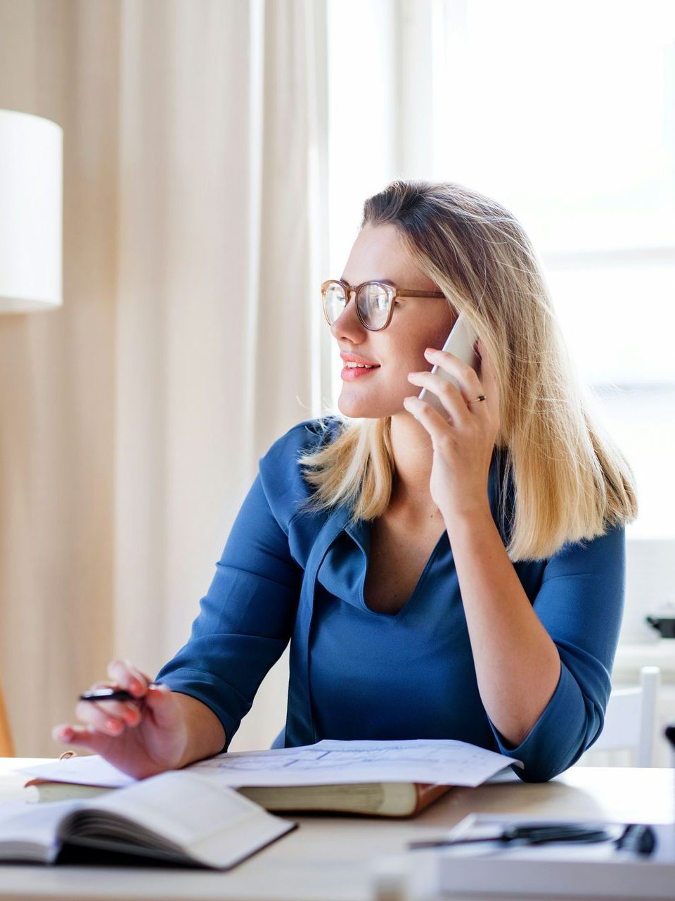 A woman is sitting at a desk talking on a cell phone.