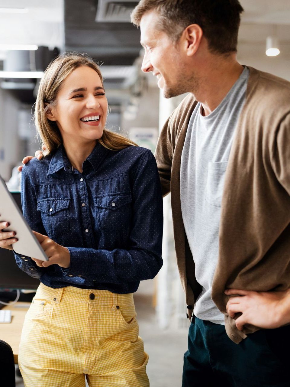 A man and a woman are laughing while looking at a tablet.