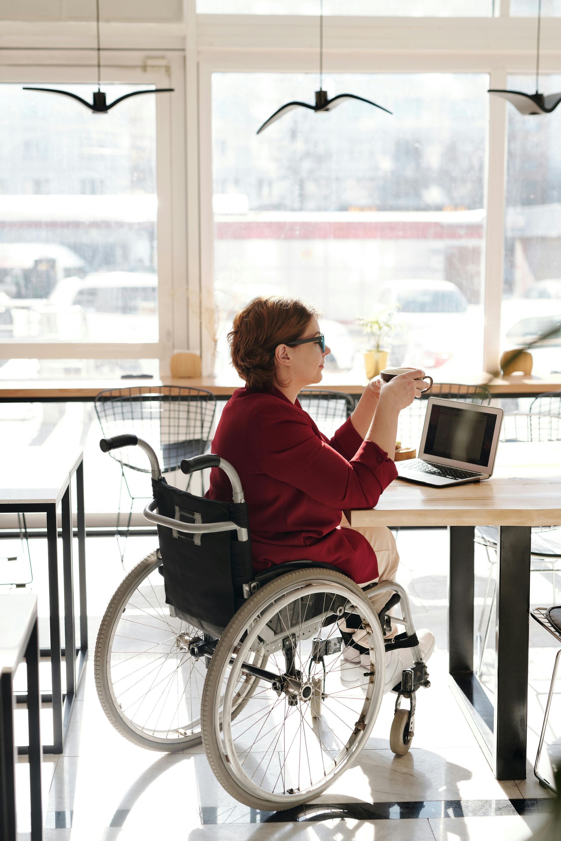 A woman in a wheelchair is sitting at a table with a laptop.