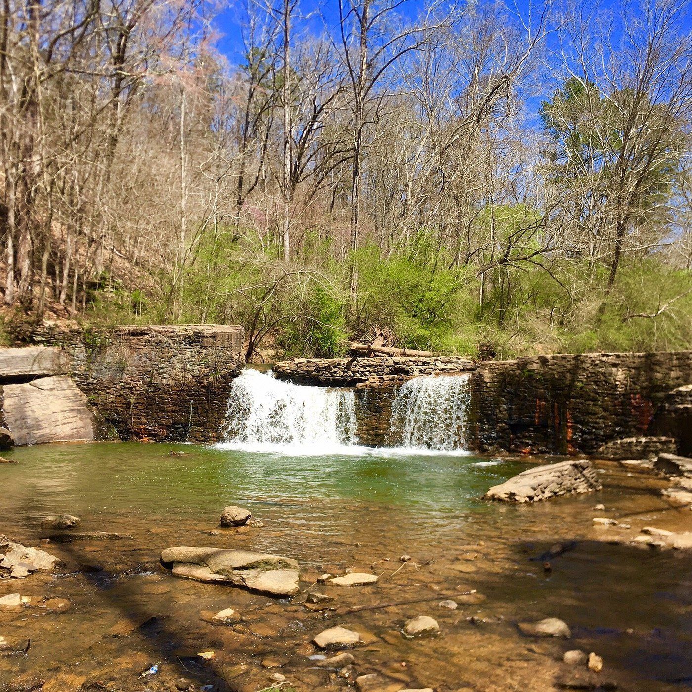 Small waterfall cascading over a stone dam into a shallow, rocky creek. Trees line the background. Water damage Lawrenceville