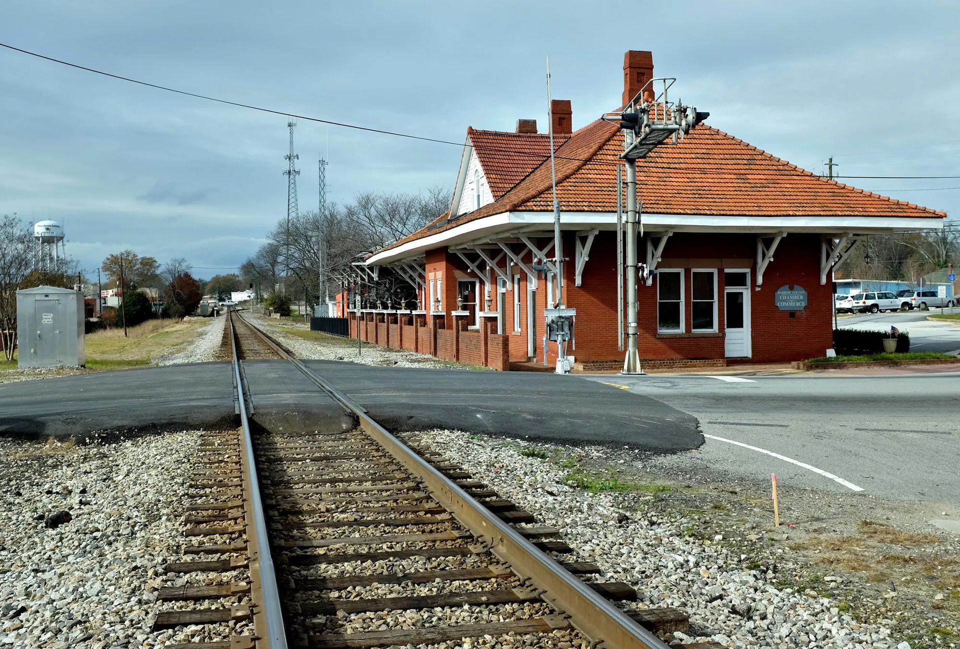 Railroad depot with red tile roof, brick walls, and tracks crossing road on a cloudy day. Plumbers in Winder Georgia.