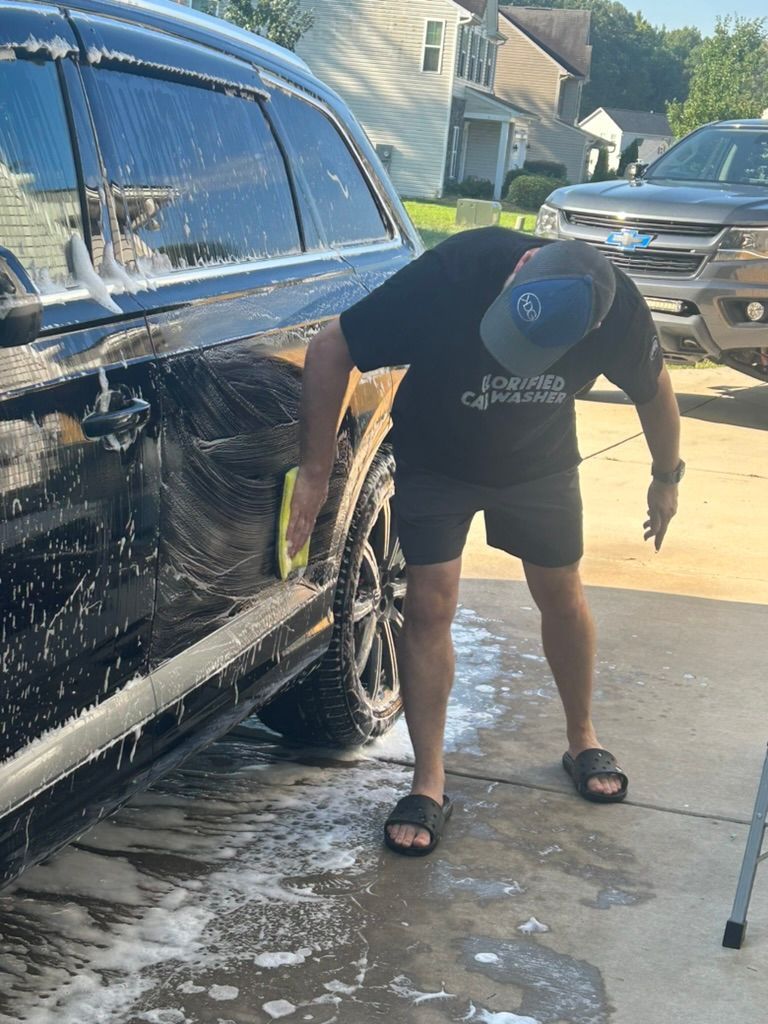 A man is washing a black suv in a driveway.
