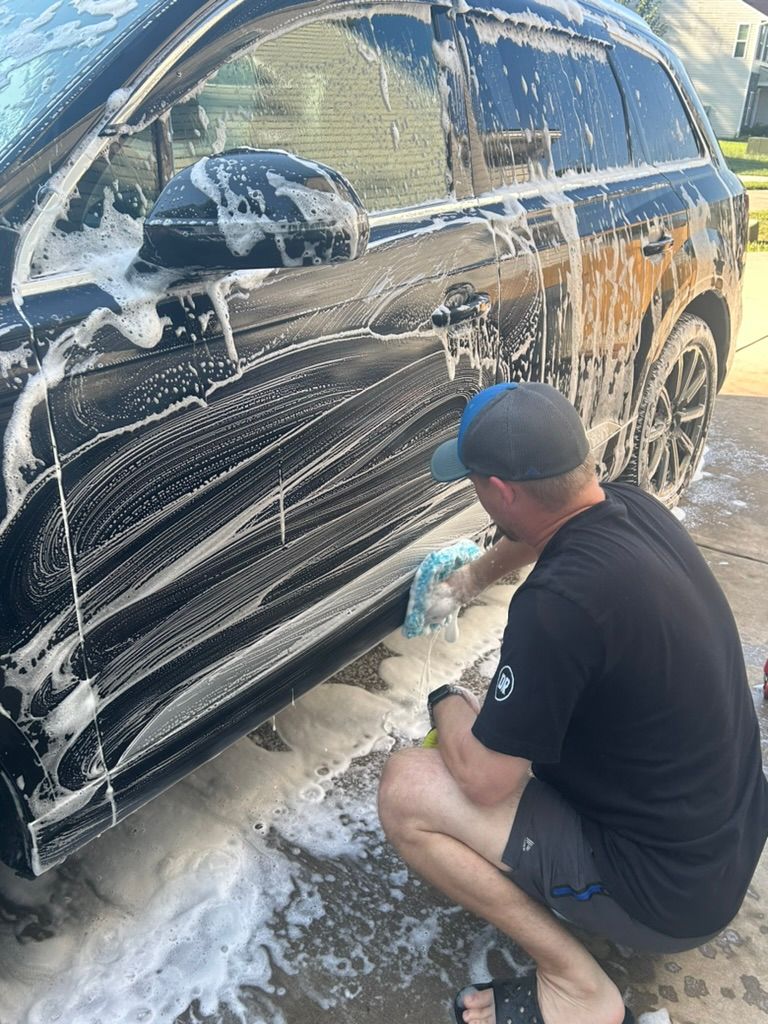 A man is kneeling down to wash a black car.