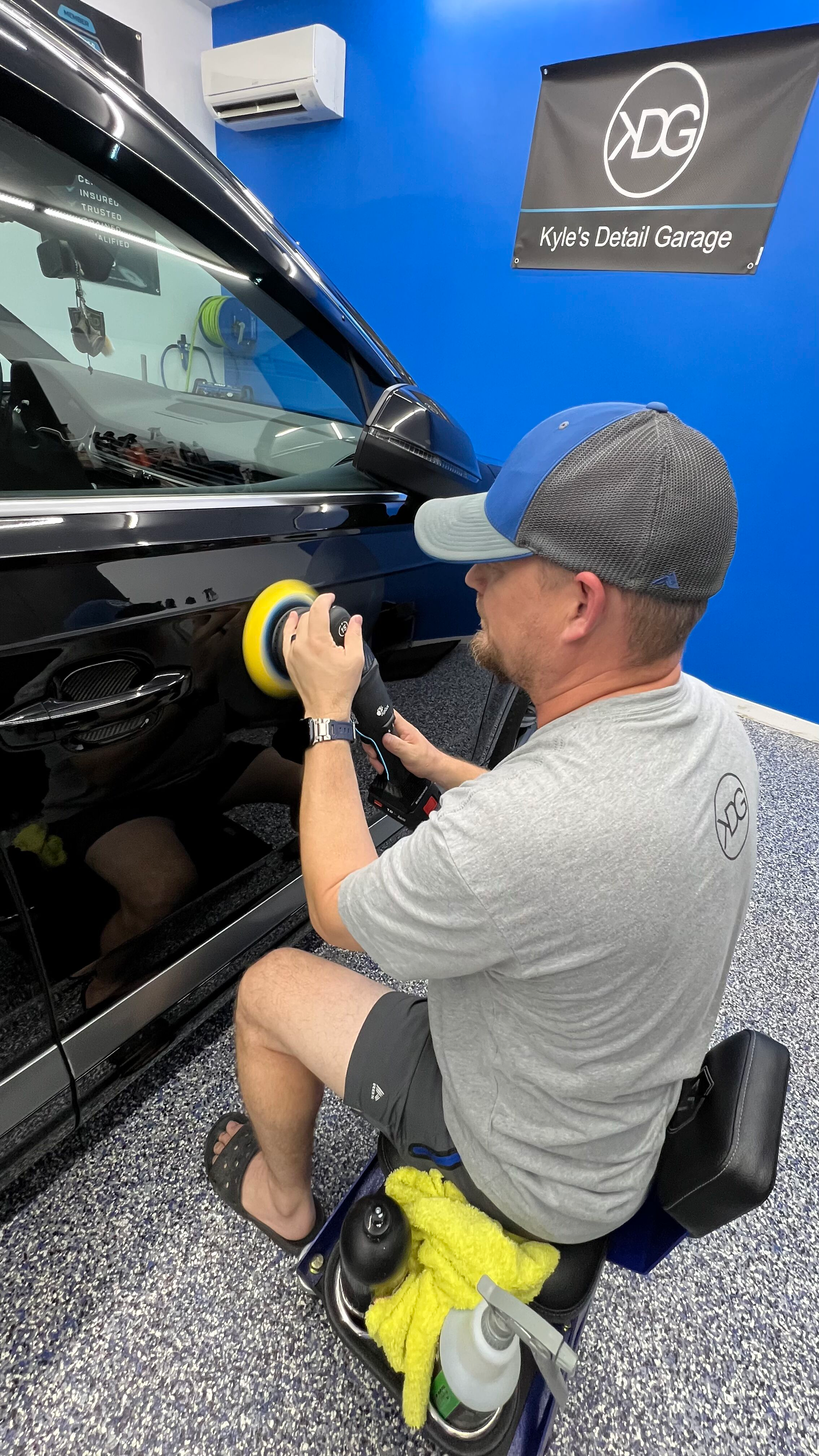 A man is sitting on a stool polishing a car.