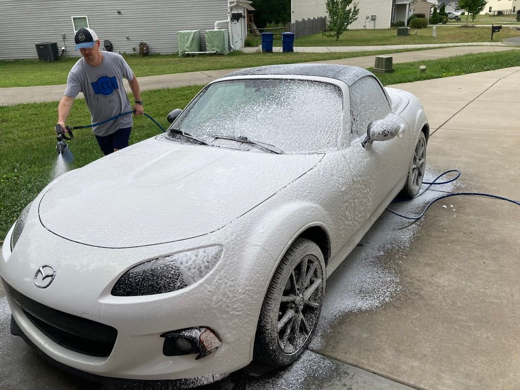 A man is washing a white sports car with a hose.