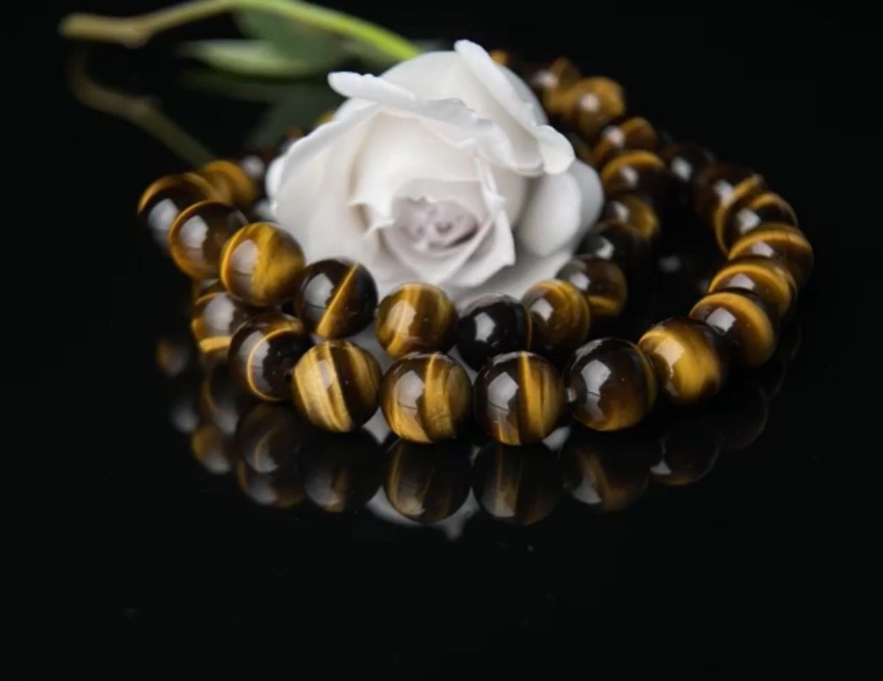 A bracelet made of tiger 's eye beads and a white rose on a black surface.