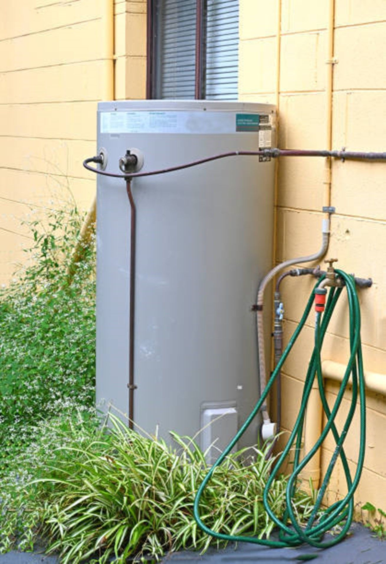 A water heater is attached to the side of a building next to a hose.