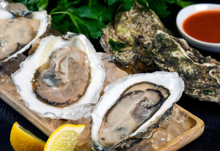 A wooden cutting board topped with oysters and lemon slices.