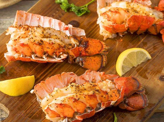 Three lobsters are sitting on a wooden cutting board with lemon slices.