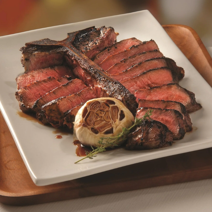 A white plate topped with steak and garlic on a wooden tray