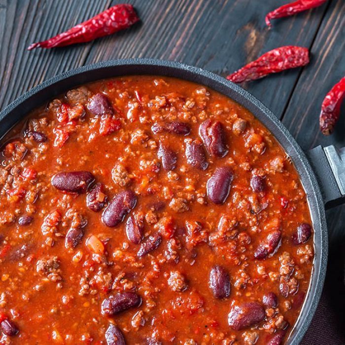 A pan filled with chili and beans on a wooden table.