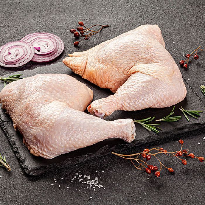 Raw chicken legs on a cutting board with onions and rosemary.
