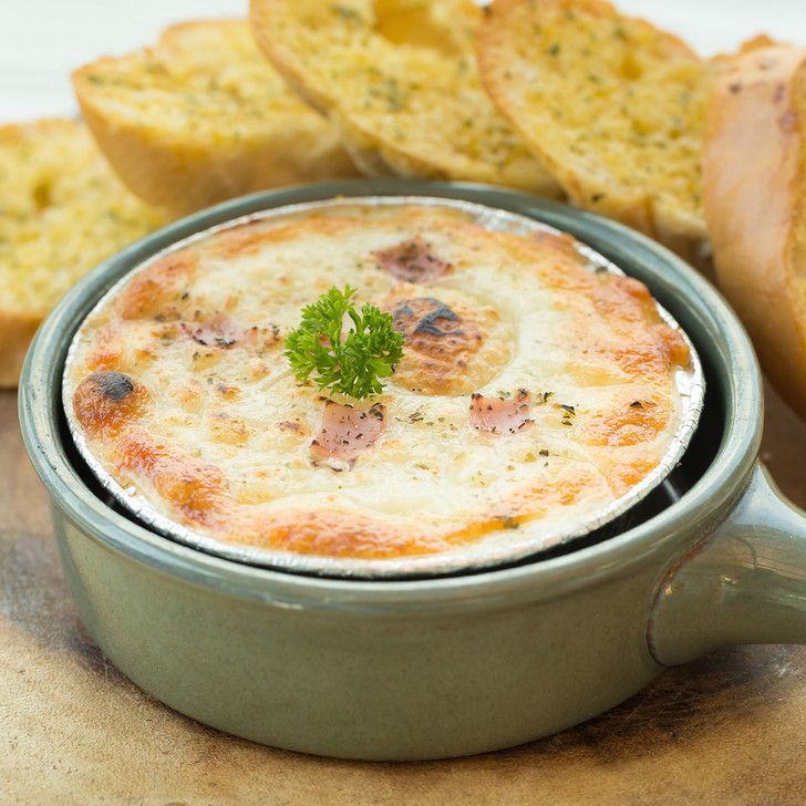 A bowl of food with garlic bread in the background