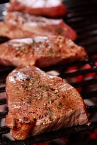 Three steaks are cooking on a grill with flames