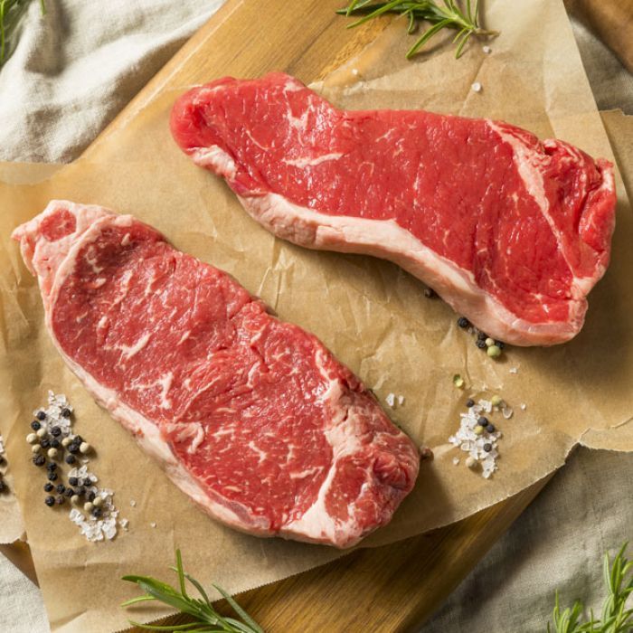Two steaks are sitting on a piece of paper on a cutting board.