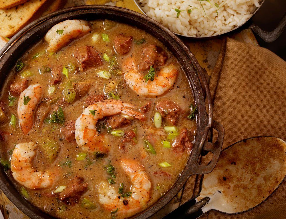 A bowl of shrimp and sausage gumbo next to a bowl of rice.
