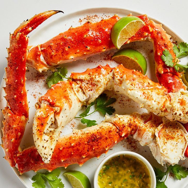 A white plate topped with crab claws , limes , cilantro and sauce.
